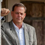 Chris Mapp leaning against a porch post outside a weathered wooden building