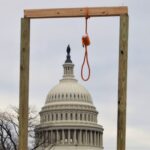 A wooden gallows with a hanging noose, erected by the crowd outside the United States Capitol, framing the Capitol dome