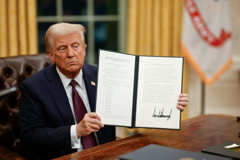 Donald Trump in the Oval Office holding up the signed Proclamation 10887, the blanket January 6 pardon, on the first night of his second term