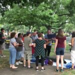 Crowds line metal barricades under the trees at the edge of Emancipation Park in Charlottesville, August 12, 2017; nationalist flags are visible among the rally-goers in the background, and cases of water are staged along the fence.