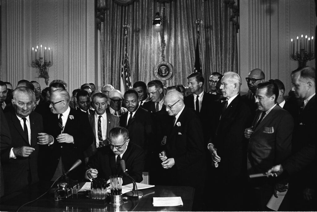 President Lyndon Johnson signing the Civil Rights Act of 1964 with Martin Luther King Jr. and others standing behind him